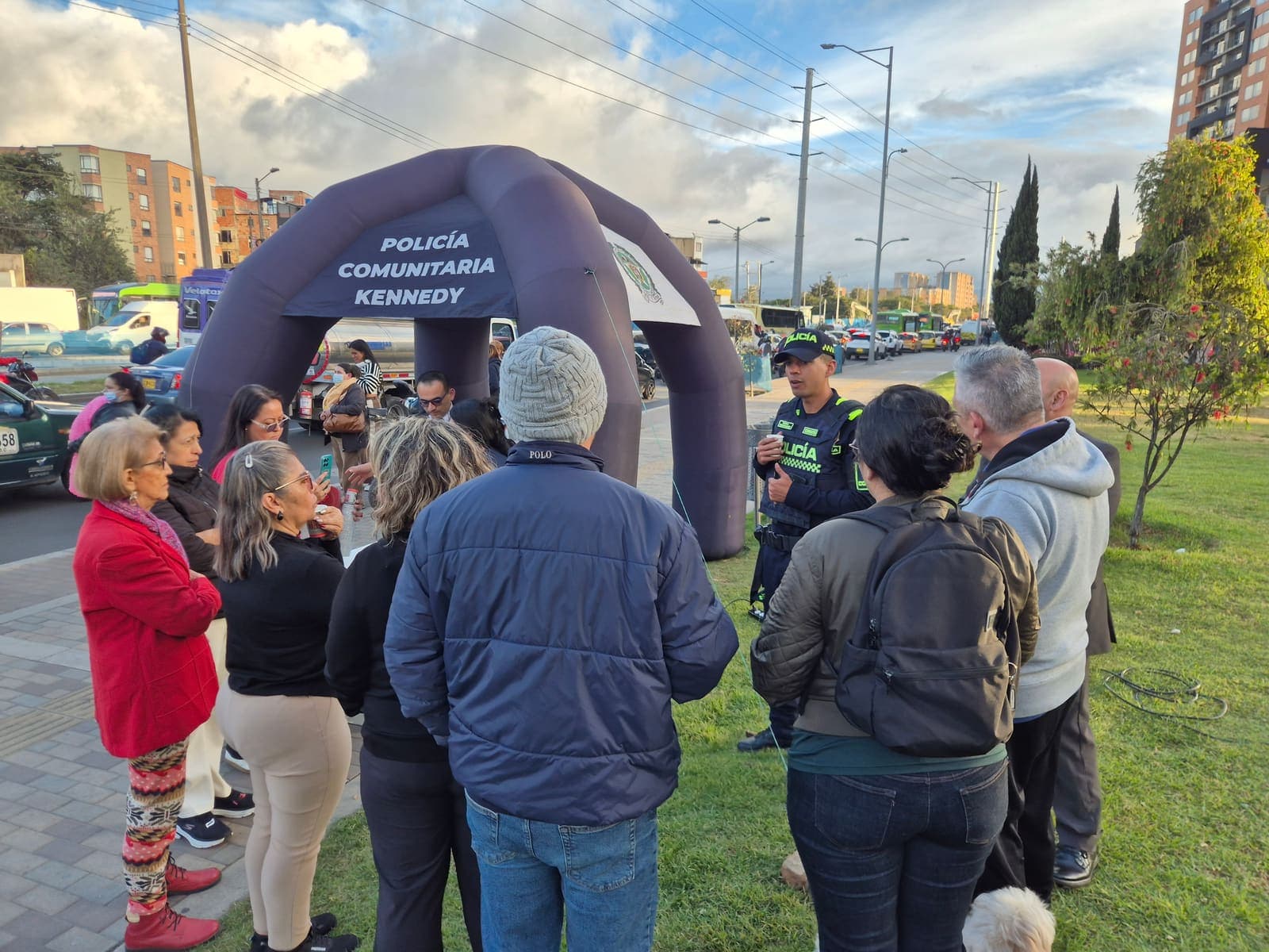 Residentes del sector reunidos en círculo alrededor de un patrullero de la Policía Comunitaria, junto al arco inflable instalado en la zona verde